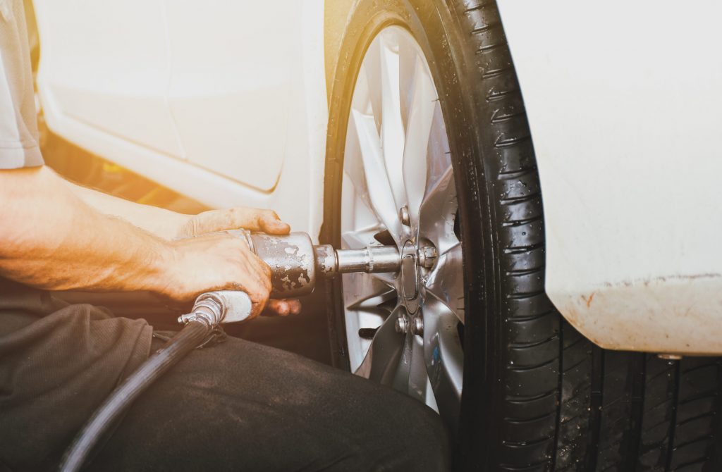 The mechanics remove the car wheel with an air impact wrench in the auto repair shop service