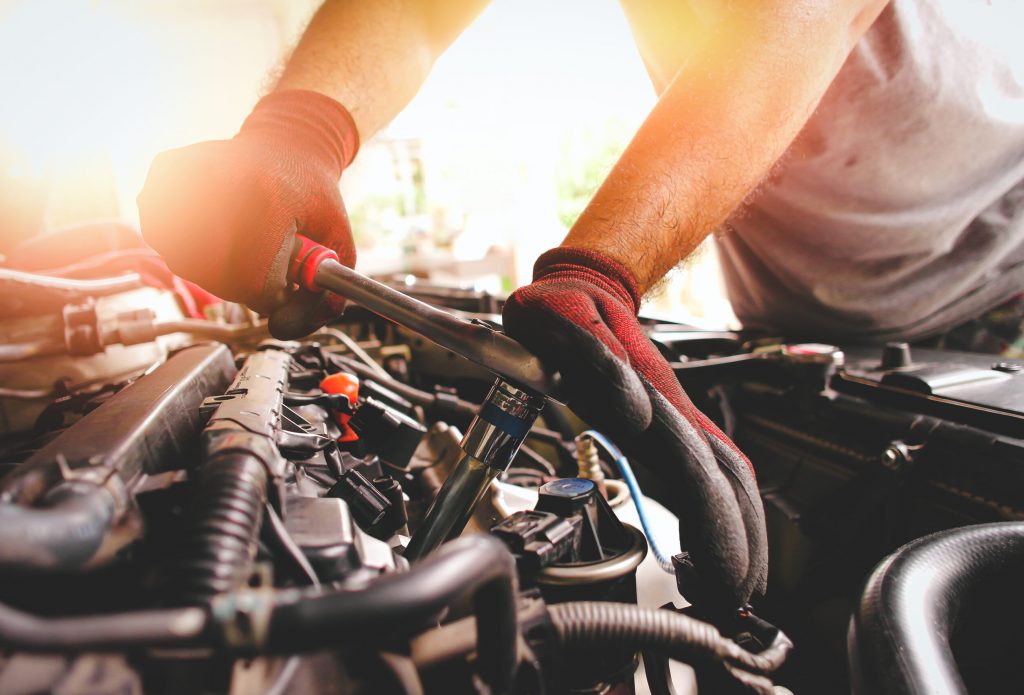 The red gloved hand of the auto mechanic is fastening the bolt w The red gloved hand of the auto mechanic is fastening the bolt with the socket wrench to fix the vehicle engine, sunlight on background